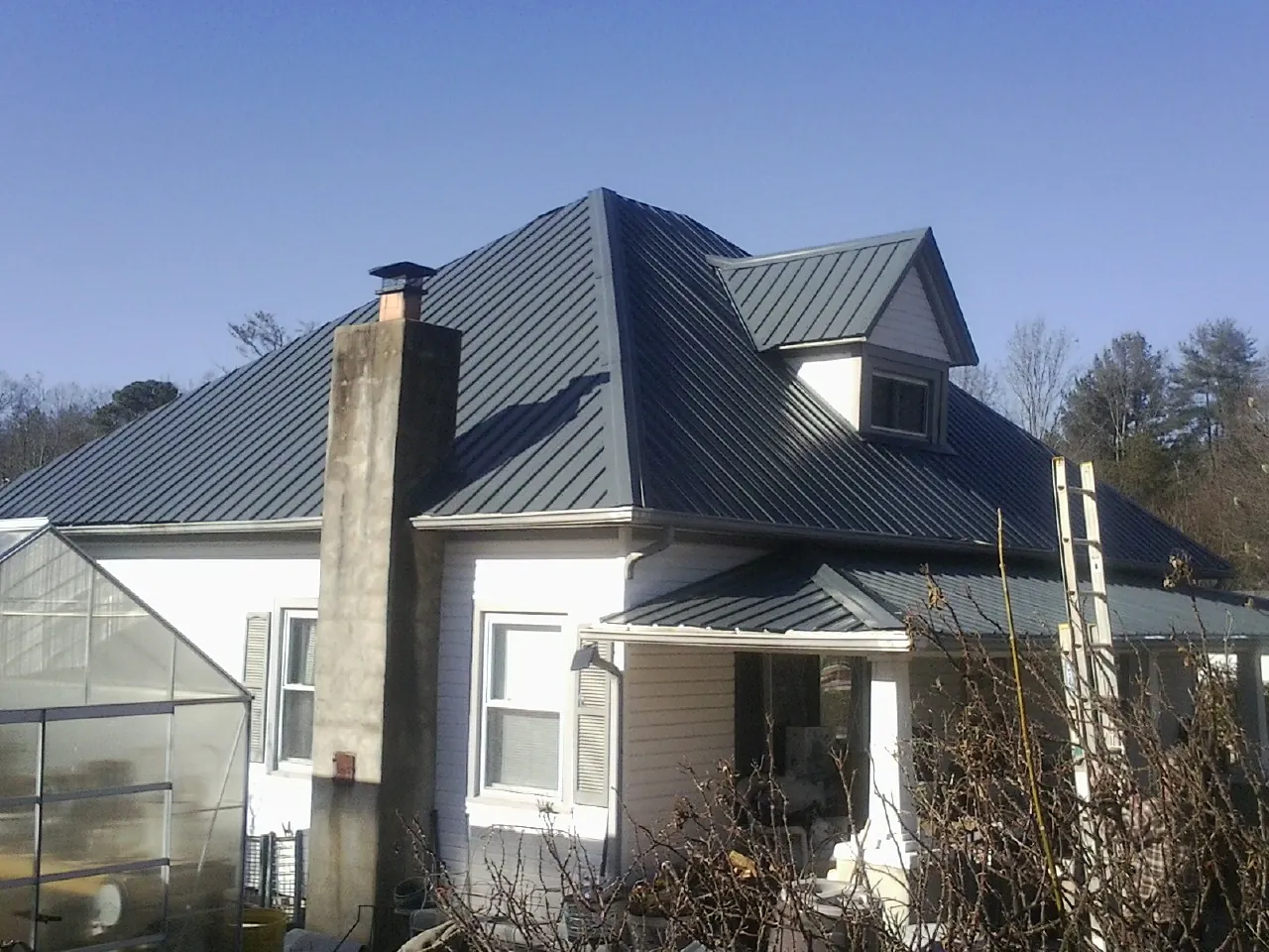 Dark blue standing seam metal roof on a white farmhouse with dormer — Slate & Tile Roof Repair by Roofing Brothers in Cheyenne