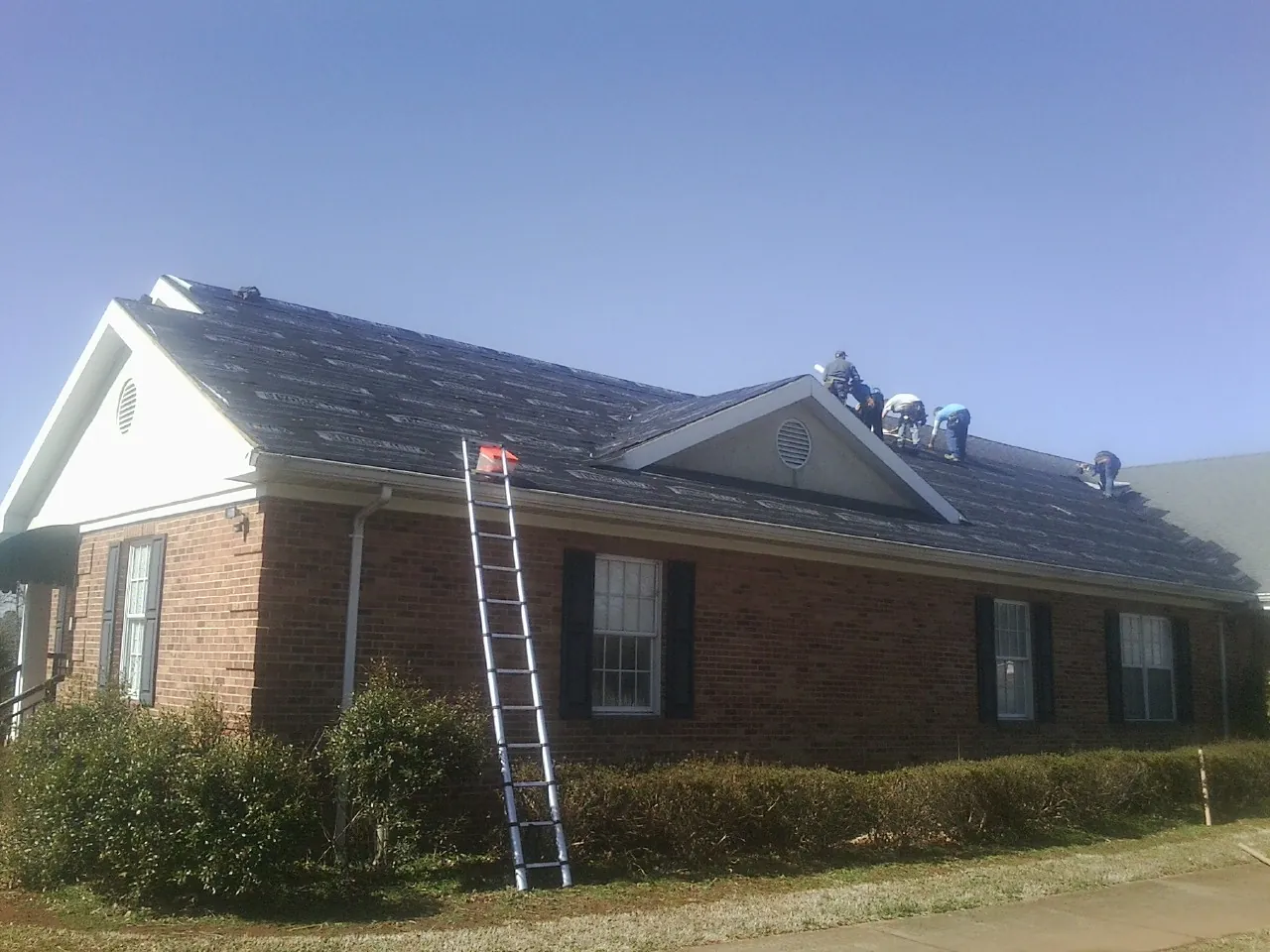 Crew tearing shingles off a brick ranch roof with a ladder set — Metal Roof Repair work by our crew in Cheyenne