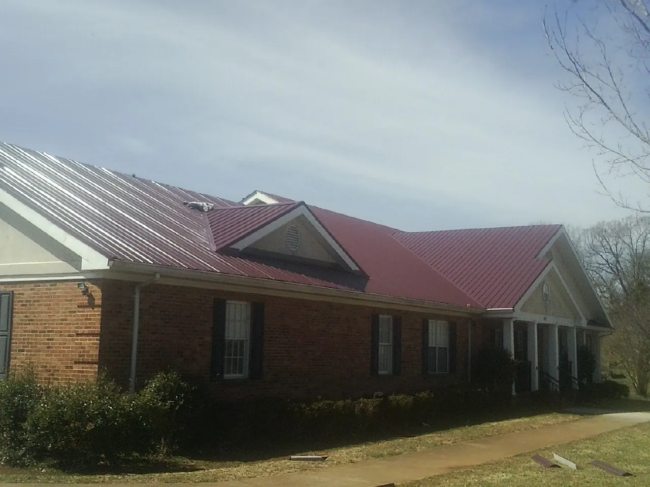 Red metal roof with gabled entries on a long brick building, from a Hail Damage Roof Repair job in Cheyenne