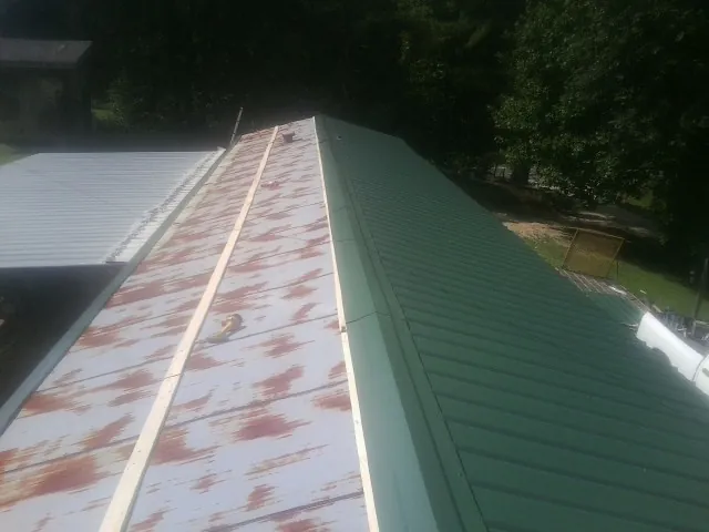 Old rusted panels beside newly installed green metal roofing — Wind Damage Roof Repair by Roofing Brothers in Cheyenne